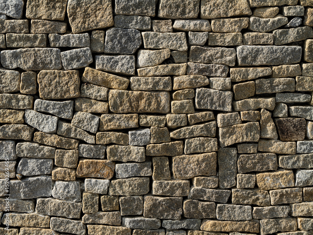 Fototapeta premium Close-up of a traditional dry stone wall with irregular stones. Rustic texture, ideal for backgrounds, architecture themes, and design mockups