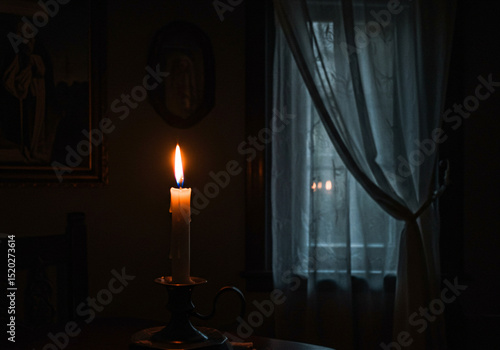 Single candle burning in dark room near window