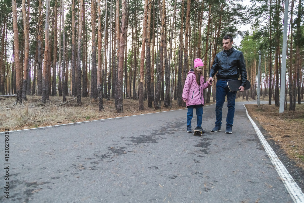 Father and daughter walking holding skateboards in their hands in the forest. Father and daughter walking holding skateboards in their hands in the forest.