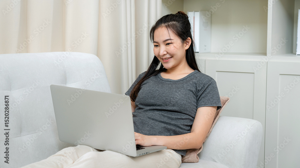 Asian freelance woman using laptop to receive email of order from client and lying on the couch to checking product on stock Asian freelance woman using laptop to receive email of order from client and lying on the couch to checking product on stock