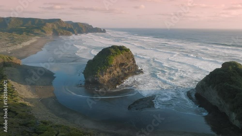 Aerial view of Bethells Beach, NZ, showcasing the rugged coastline, lush green cliffs, and powerful waves crashing against the shore. A popular destination for surfers and nature lovers.	