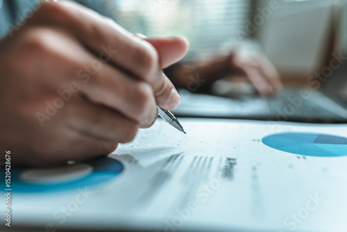 A close-up view of a businessman hand gripping a pen, indicating a project along with financial report on paper document, symbolizing data analysis, corporate, team and business strategy planning.