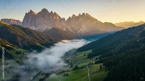 A stunning aerial view captures a misty mountain valley at sunrise, with a village nestled below jagged, glowing peaks, surrounded by lush green slopes 2K Quad HD QHD Quality 8 seconds 