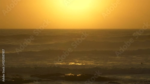Soft, hazy sunset over the ocean on the coast of Portugal. Warm summer evening with bright orange sky and setting sun on the horizon.