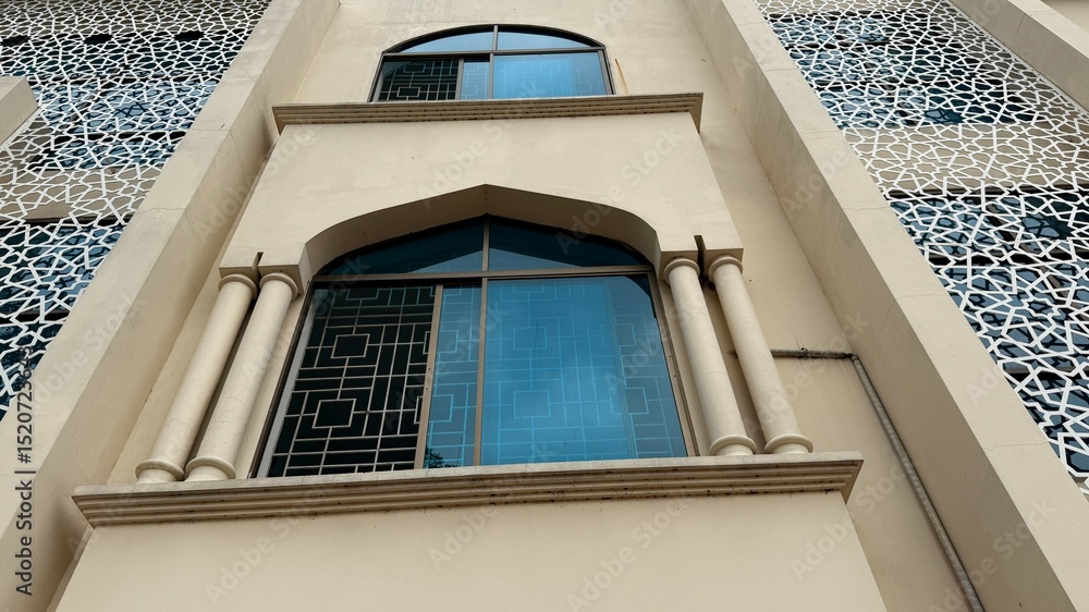 Fototapeta premium Beige Building with Arched Windows, Pillars, and Geometric Screen Details Low Angle View