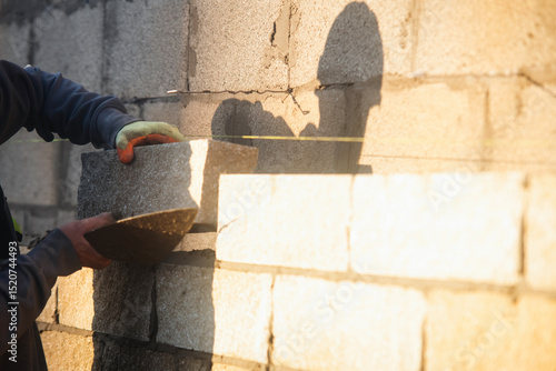 Fotografija Bricklayer constructing stone wall using stone blocks, cement mortar mix and tro