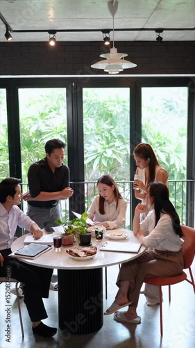 A team of young Asian professionals holds a productive lunch meeting in a cozy, light-filled home office with plants and elegant furnishings.