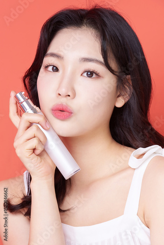 Young Asian Woman Holding Skincare Serum Bottle on Coral Background