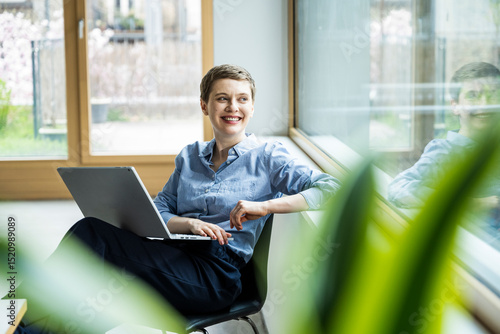 Businesswoman in office with laptop smiling and looking away