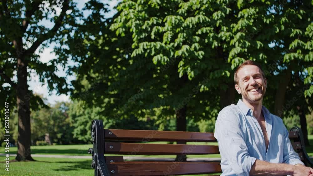 Cheerful male sitting on park bench, radiating pure joy while basking in warm sunlight and natural surroundings during leisurely summer day Cheerful male sitting on park bench, radiating pure joy while basking in warm sunlight and natural surroundings during leisurely summer day