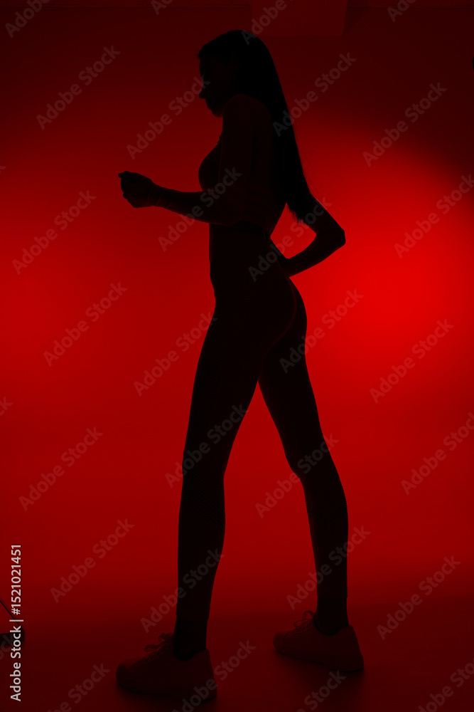 Fototapeta premium Silhouette of a woman sport fitness figure with athletic posture, dark lighting, and red background creating a striking, dynamic mood for health and exercise themes.