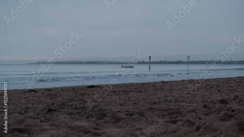 EDINBURGH, SCOTLAND, UK - JANUARY 5, 2024: Tranquility of Portobello Beach at sunrise with cloudy skies and rowing boat gently gliding across the still waters of Edinburgh.