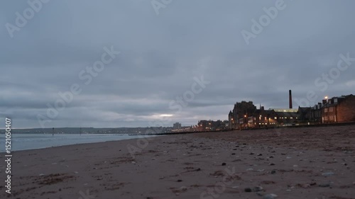 Serene morning at Portobello Beach with a cloudy sunrise reflecting, while the shoreline glimmers in the dawn light, night city.