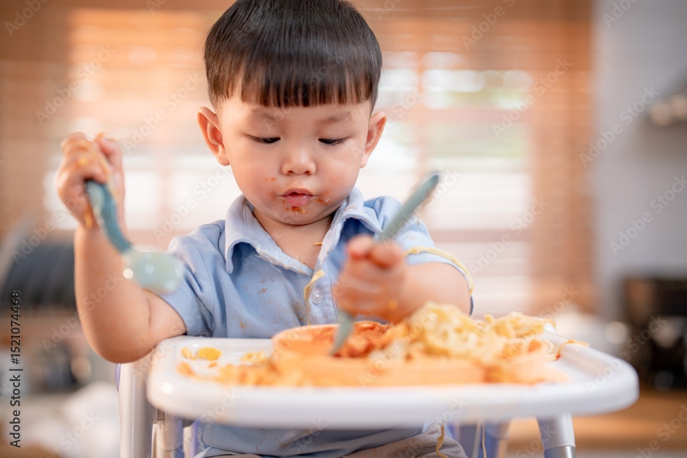 Young child enjoys messy mealtime with spaghetti and sauce in a cozy kitchen Young child enjoys messy mealtime with spaghetti and sauce in a cozy kitchen