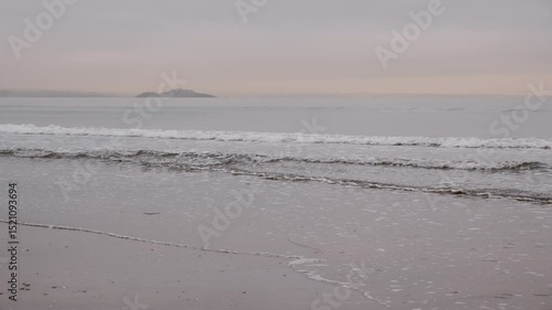 EDINBURGH, SCOTLAND, UK - JANUARY 5, 2024: Tranquil atmosphere of Portobello Beach in Edinburgh as clouds soften the sunrise over gentle waves, bringing peace to the coast, island in the mist on the