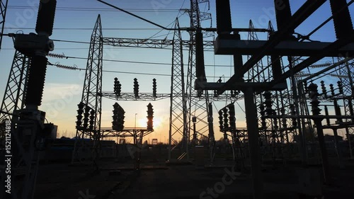 Silhouettes of electrical parts and structural elements of a power plant at sunset. the sun appears and disappears through the structure due to the movement of the camera.