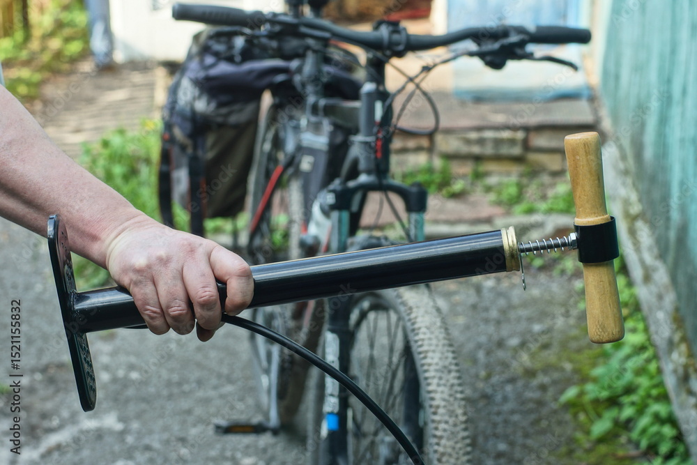 Obraz premium man holding in hand one iron with wooden handle industrial black new with rubber hose and clamp long car with spring pump daytime on street near bicycle