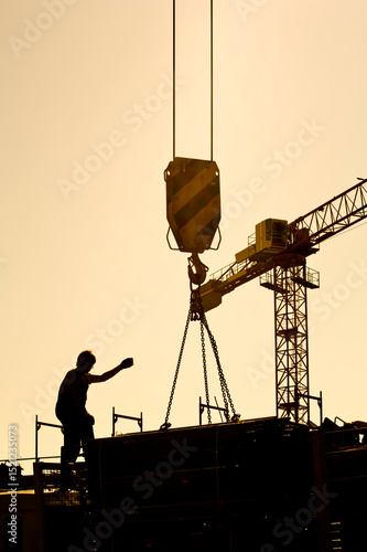 silhouette of construction worker conducting crane lifting load