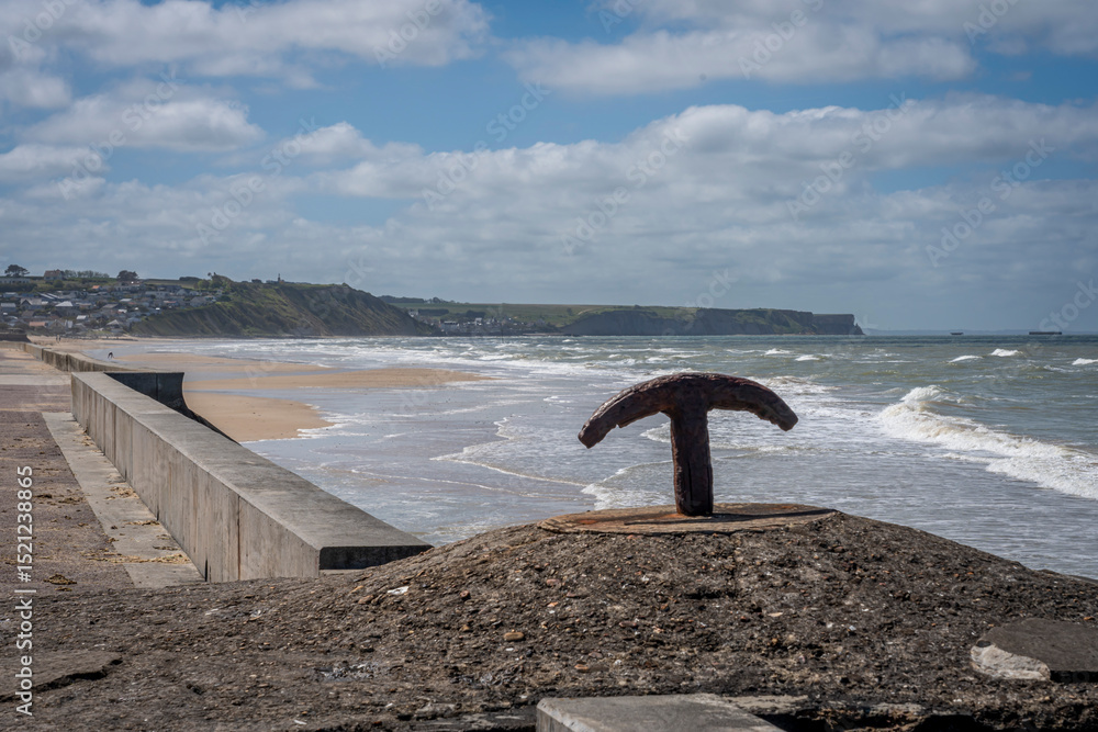 Fototapeta premium Asnelles-Sur-Mer, France - 05 16 2025: Panoramic view of the Seaside dike, the sea, the beach, cliffs and pontoons behind
