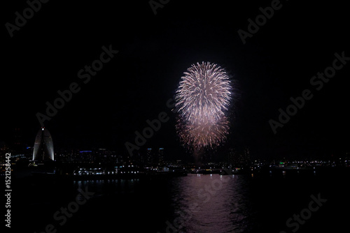 Fireworks explode in the sky over Yokohama Port, with the city skyline in the background