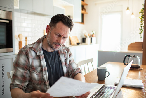 Wall Mural Man looking stressed while reviewing bills at home office