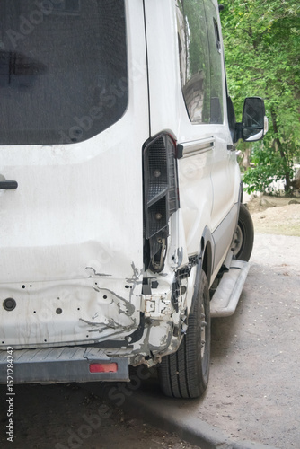 Damage to the rear of a white van parked on a roadside in a green area during daytime after a collision incident