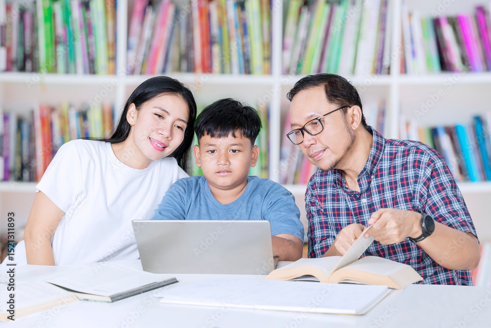 Asian Family Helping Son Study with Laptop and Books in Home Library Asian Family Helping Son Study with Laptop and Books in Home Library