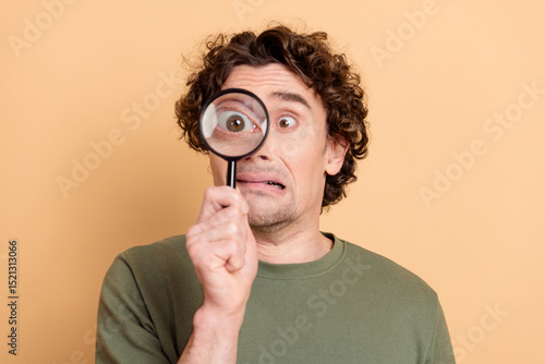 Canvas Print Young man with curly hair holding magnifying glass displaying a surprised expres