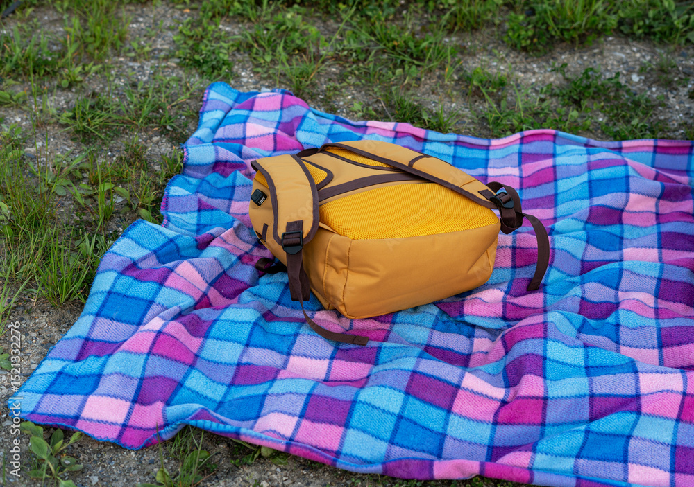 Naklejka premium yellow backpack lying on checkered blue blanket on the ground, tourism and hiking concept, outdoor recreation