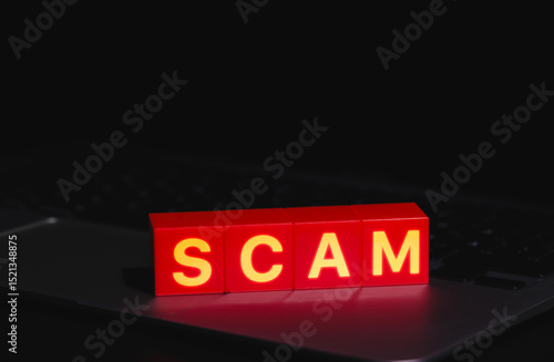 Red Scam Blocks Highlighting Cyber Fraud. Spelling SCAM placed on laptop keyboard in dark environment, symbolizing cyber fraud, phishing, scammer, cybersecurity threats, and online deception risks.