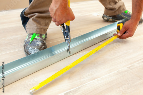 Tableau sur toile Construction worker cutting metal profile with aviation snips and measuring with