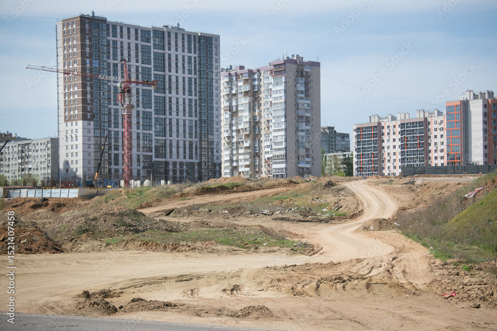 construction of the foundation of a new residential building using a tower crane in a large neighborhood with new tall modern multi-storey buildings on the background of which a winding dirt road lead construction of the foundation of a new residential building using a tower crane in a large neighborhood with new tall modern multi-storey buildings on the background of which a winding dirt road lead