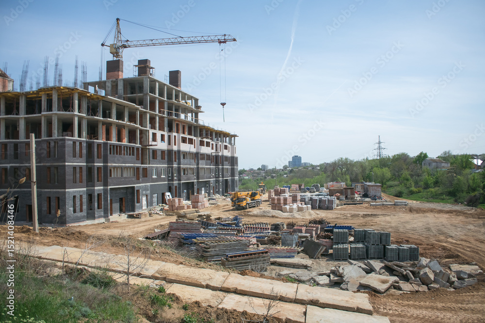 Fototapeta premium construction site with a warehouse of building materials and a tower crane, which is used to build a new large multi-storey brick apartment building