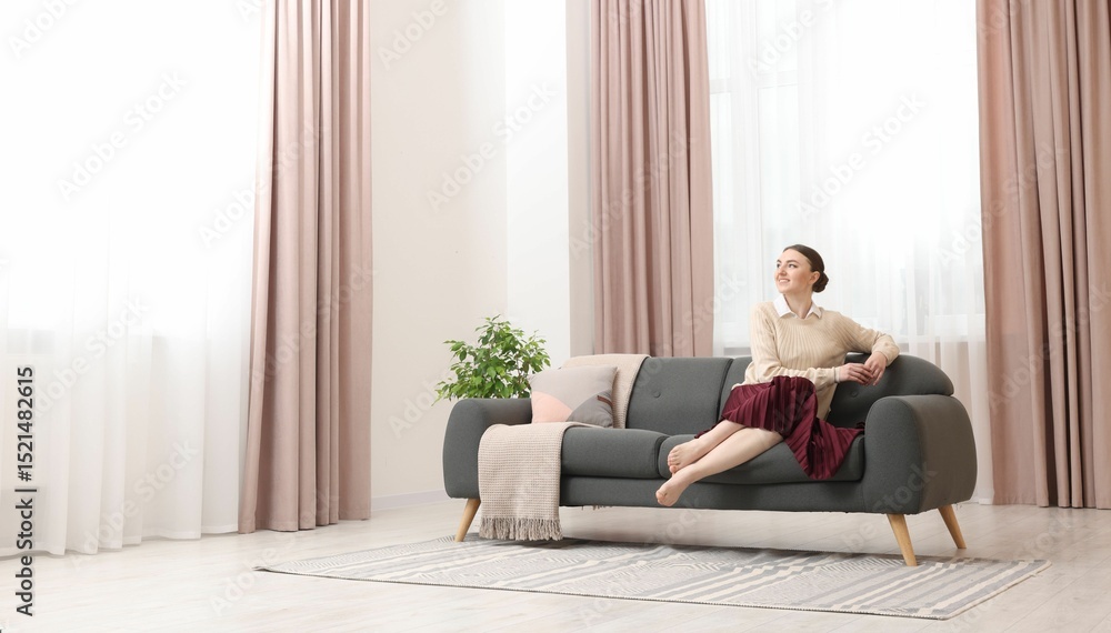 Woman sitting on sofa near window with stylish curtains at home. Space for text Woman sitting on sofa near window with stylish curtains at home. Space for text