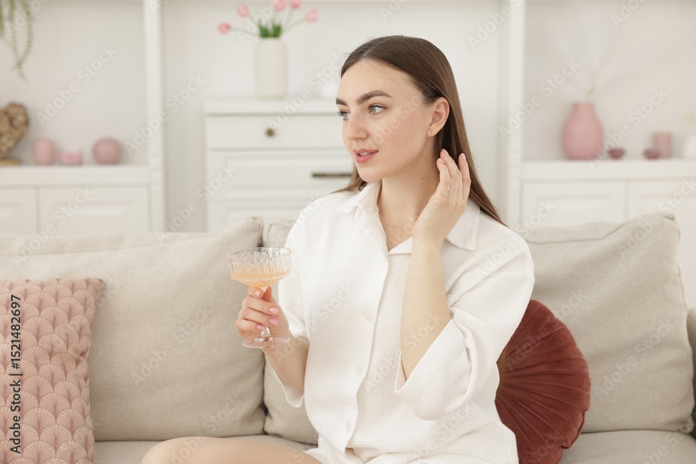 Beautiful woman with glass of alcoholic drink sitting on sofa at home Beautiful woman with glass of alcoholic drink sitting on sofa at home
