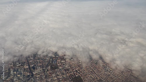 Aerial view of Munich, Germany, with the city partially covered by thick clouds and fog, revealing detailed urban patterns and the Olympic Tower piercing the cloud layer