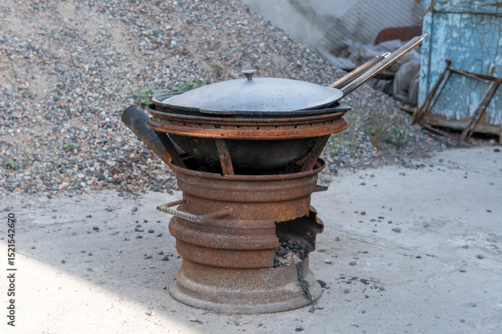 Steel kazan, a large cast iron cauldron, on a fire pit for cooking outdoors. Outdoor cooking concept with wood burning stove Steel kazan, a large cast iron cauldron, on a fire pit for cooking outdoors. Outdoor cooking concept with wood burning stove