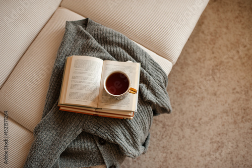 Cup of black tea staying on open paper books with knitted textile on white velvet couch  in living room at home. Cozy and hygge atmosphere. Coziness.