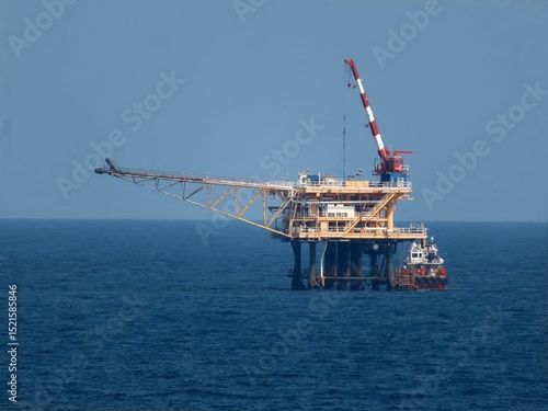 Offshore oil platform stands tall against a vast, deep blue ocean under a clear sky. A support vessel is nearby, ensuring safe operations in the maritime environment.