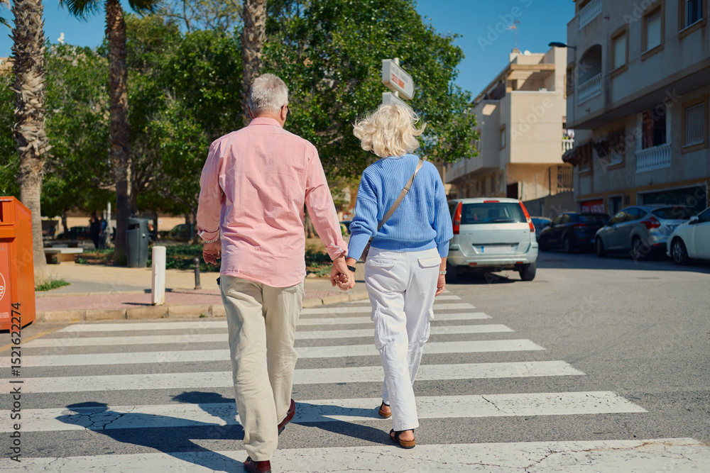 Elderly couple walking hand in hand across a crosswalk in a sunny neighborhood Elderly couple walking hand in hand across a crosswalk in a sunny neighborhood