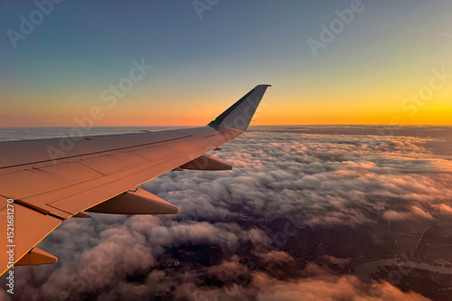 Fototapeta Naklejka Na Ścianę i Meble -  Wing of an airplane above clouds and land at sunset