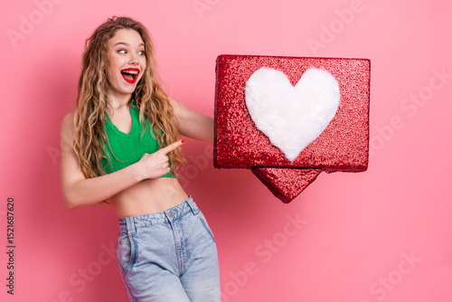 Cheerful young woman holding a glittery red gift box with a heart symbol in front of a vibrant pink background.