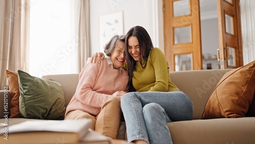 Charming Caucasian mother or grandmother placing head on girls shoulder. Joyful young female hugging her loving relative. Comfortably sitting on couch and positively looking at camera. Family concept