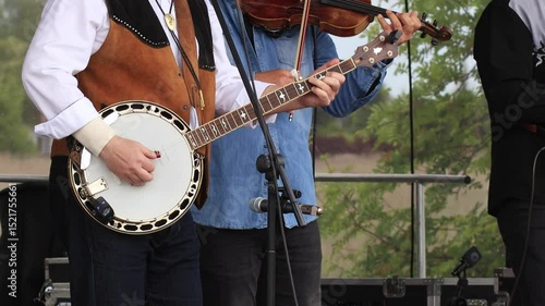 Close-up of a bluegrass band playing live. Musicians in Western outfits perform with banjo, violin, and mandolin during an outdoor country music concert.