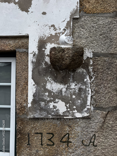 Tableau sur toile A mud swallow nest built on a rustic stone wall beneath a small white swan figurine, above the year 1734 engraved on a historic building along the Camino de Santiago, Spain