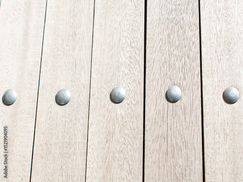 A photo of a close-up of a wooden surface composed of vertical planks. Each plank has a light, almost whitewashed wood grain appearance. Along the middle of the image, evenly spaced across the p