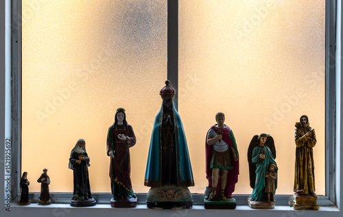 Statues of Catholic saints on a windowsill, including Our Lady of Aparecida, Saint George and others — symbols of Brazil's religious traditions and popular devotions.