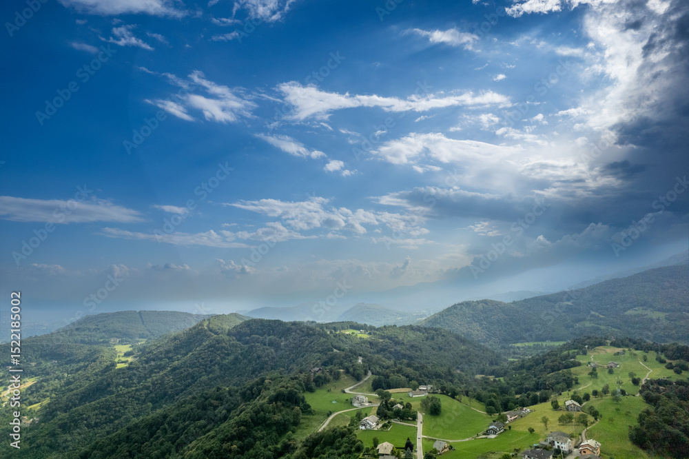 Fototapeta premium Drone panorama of the Ivrea Morainic Amphitheatre seen from Brosso, Val Chiusella, Italy, showing lush green plains, woods, and scattered villages under clear sky, high drone shot, slow motion