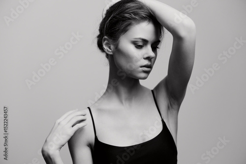 Elegant woman posing with a thoughtful expression, highlighting her graceful posture against a soft gray backdrop. Black and white art portrait showcasing beauty.