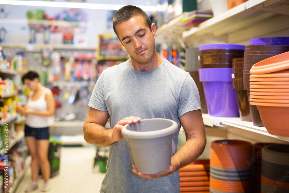 Caucasian man standing at shelf in supermarket and choosing plant pot. Caucasian man standing at shelf in supermarket and choosing plant pot.